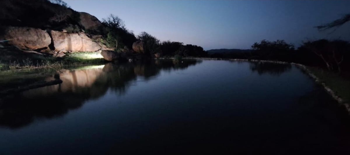 The floodlit waterhole and rocks reflected in still water after dark